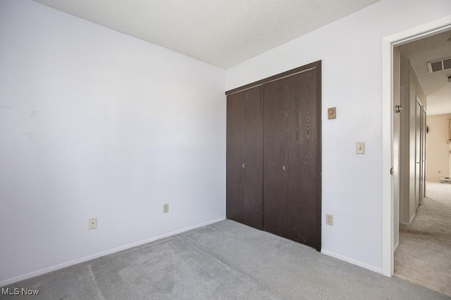 unfurnished bedroom with visible vents, light colored carpet, a closet, and baseboards