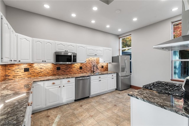 kitchen featuring backsplash, dark stone counters, stainless steel appliances, wall chimney exhaust hood, and a sink