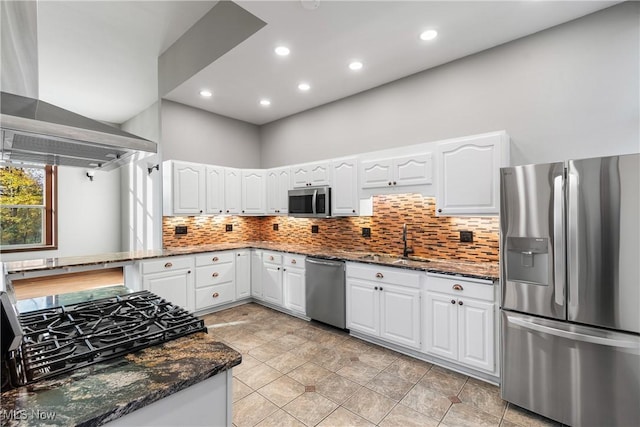 kitchen featuring dark stone countertops, stainless steel appliances, wall chimney range hood, and a sink