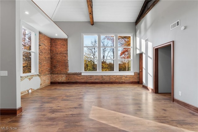 spare room featuring beam ceiling, visible vents, brick wall, and wood finished floors