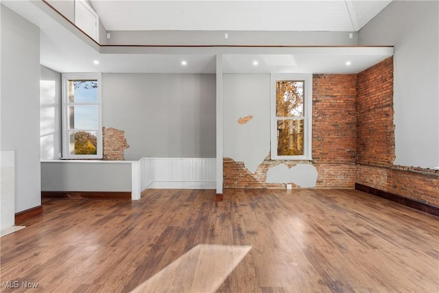 unfurnished room with wood finished floors, plenty of natural light, brick wall, and recessed lighting