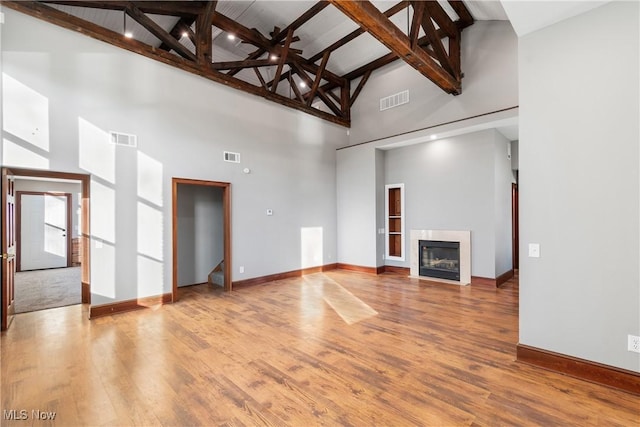 unfurnished living room with visible vents, wood finished floors, and a glass covered fireplace