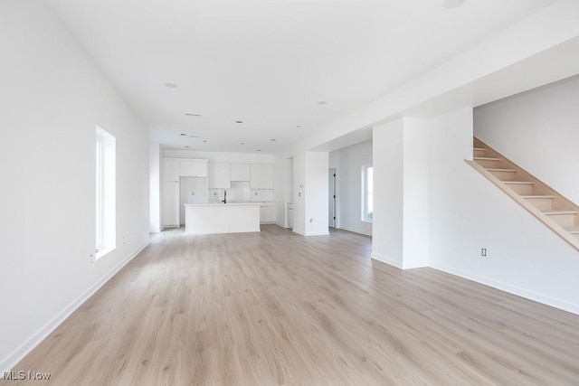 unfurnished living room with light wood finished floors, stairs, and baseboards