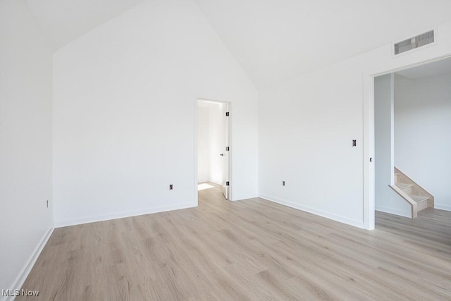 unfurnished room with light wood-type flooring, visible vents, baseboards, and high vaulted ceiling