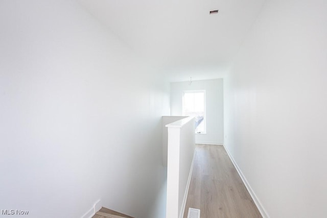 hall with light wood-type flooring, visible vents, an upstairs landing, and baseboards