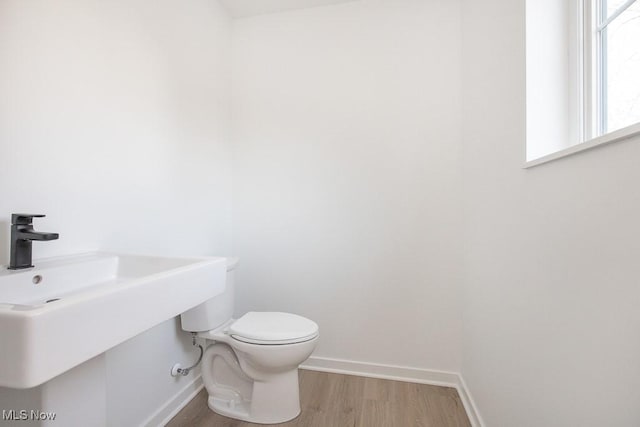 half bathroom with a sink, baseboards, toilet, and wood finished floors