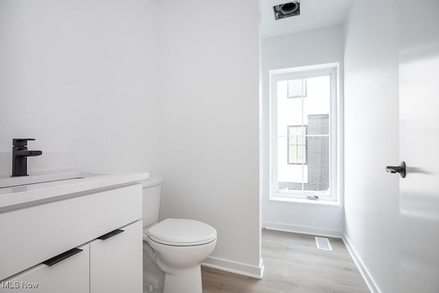 half bathroom with visible vents, baseboards, toilet, wood finished floors, and vanity