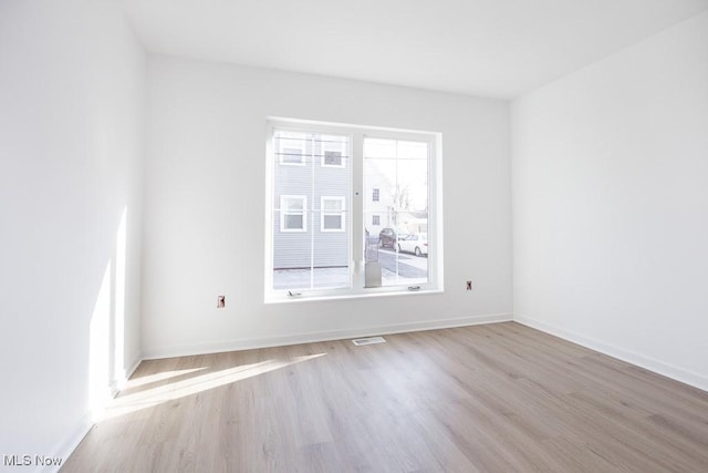 spare room featuring a wealth of natural light, visible vents, baseboards, and wood finished floors