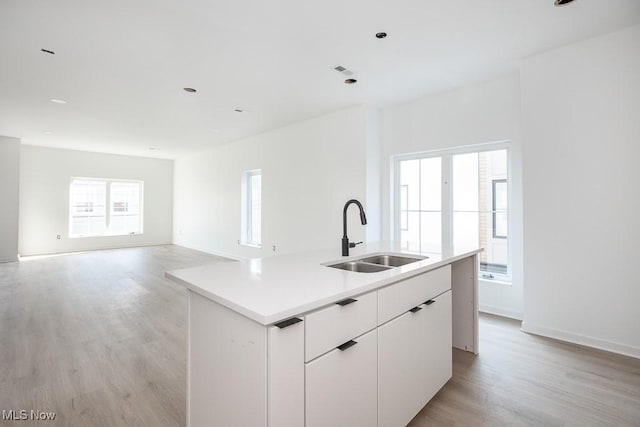 kitchen with light wood finished floors, an island with sink, a sink, light countertops, and white cabinets