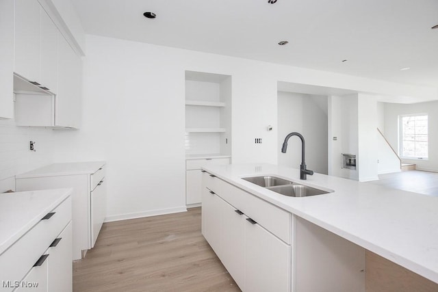 kitchen featuring light countertops, white cabinets, light wood finished floors, and a sink