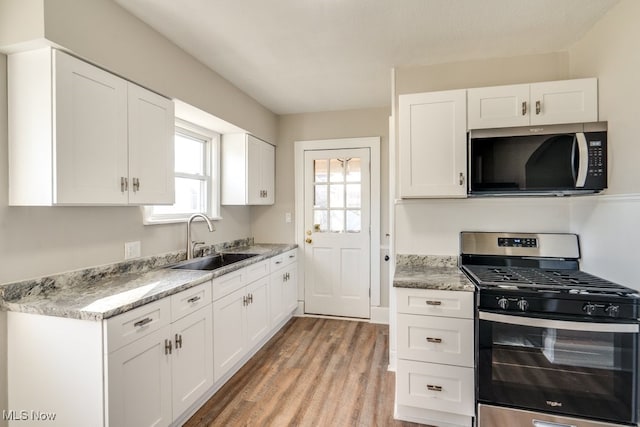 kitchen with light stone countertops, light wood finished floors, a sink, stainless steel appliances, and white cabinetry