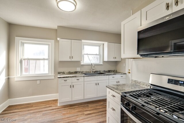 kitchen featuring baseboards, light wood finished floors, a sink, appliances with stainless steel finishes, and white cabinetry