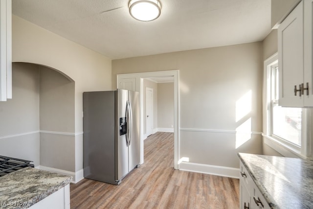 kitchen with white cabinets, baseboards, stainless steel refrigerator with ice dispenser, and light wood-type flooring