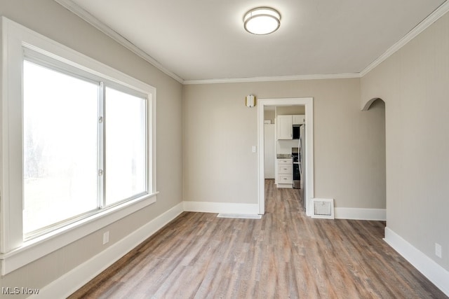 unfurnished room with visible vents, baseboards, wood finished floors, and ornamental molding