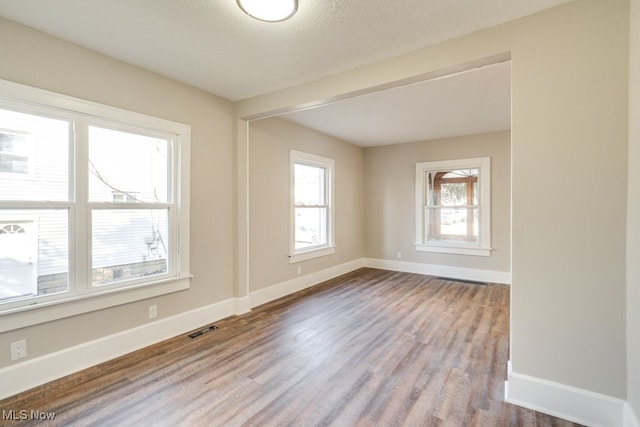 empty room with visible vents, baseboards, a textured ceiling, and wood finished floors