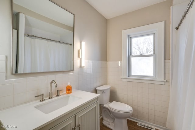 bathroom featuring visible vents, a wainscoted wall, toilet, vanity, and tile walls