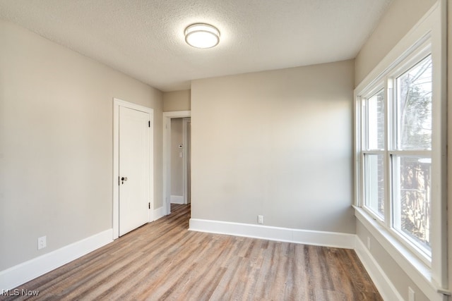 empty room featuring a textured ceiling, baseboards, and wood finished floors