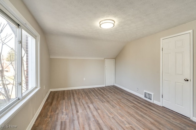 additional living space with visible vents, lofted ceiling, a textured ceiling, wood finished floors, and baseboards