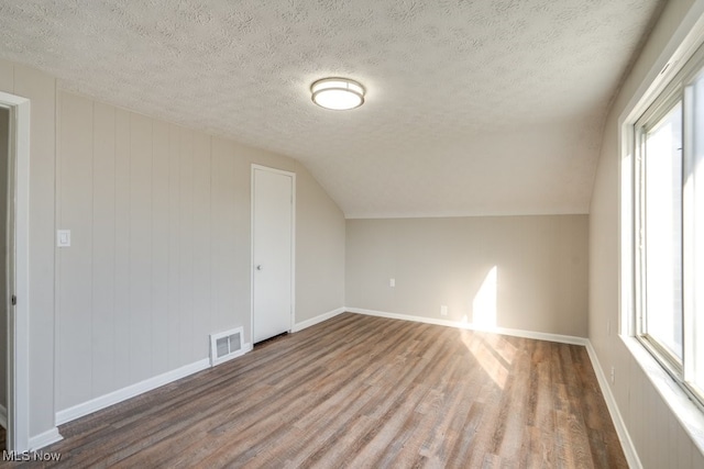 additional living space with wood finished floors, baseboards, visible vents, lofted ceiling, and a textured ceiling