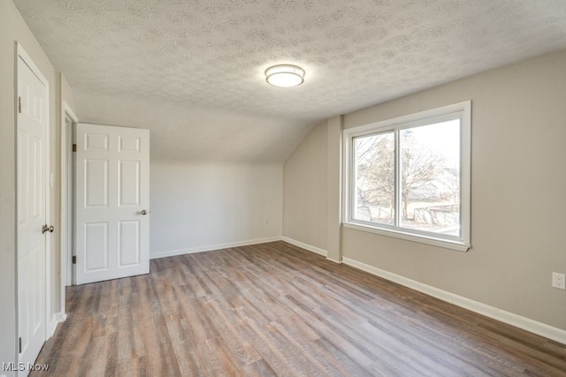 additional living space featuring baseboards, a textured ceiling, lofted ceiling, and wood finished floors