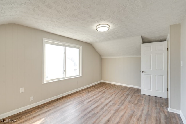 bonus room with vaulted ceiling, wood finished floors, baseboards, and a textured ceiling