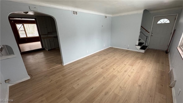 unfurnished living room featuring visible vents, wood finished floors, stairway, arched walkways, and baseboards