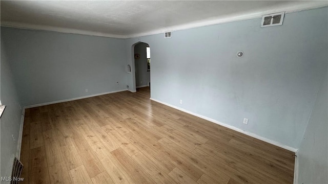 spare room featuring visible vents, arched walkways, baseboards, and wood-type flooring