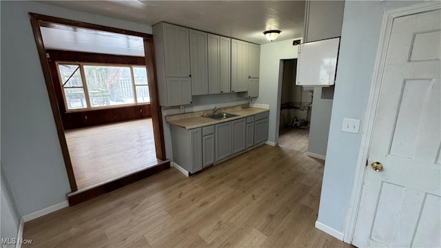 kitchen with a sink, light wood-style floors, gray cabinets, and light countertops