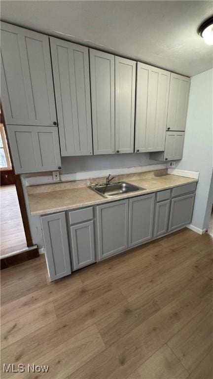 kitchen with light wood-style flooring, gray cabinetry, and a sink