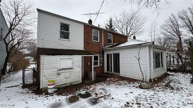 snow covered rear of property featuring fence, brick siding, and a chimney