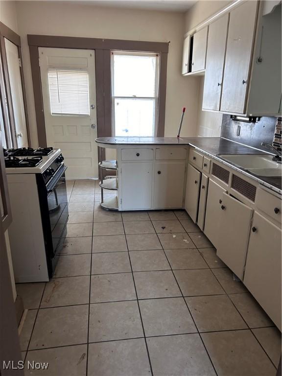 kitchen featuring black range with gas stovetop, a peninsula, light tile patterned flooring, white cabinetry, and a sink