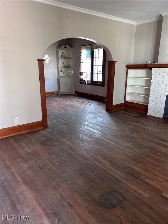 empty room featuring dark wood-style floors, arched walkways, a fireplace, crown molding, and baseboards