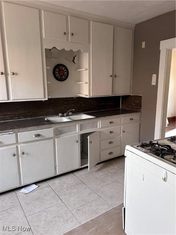 kitchen featuring light tile patterned floors, a sink, white cabinetry, dark countertops, and white gas range