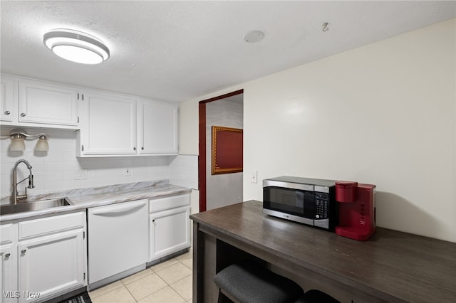 kitchen with white dishwasher, a sink, white cabinets, stainless steel microwave, and tasteful backsplash