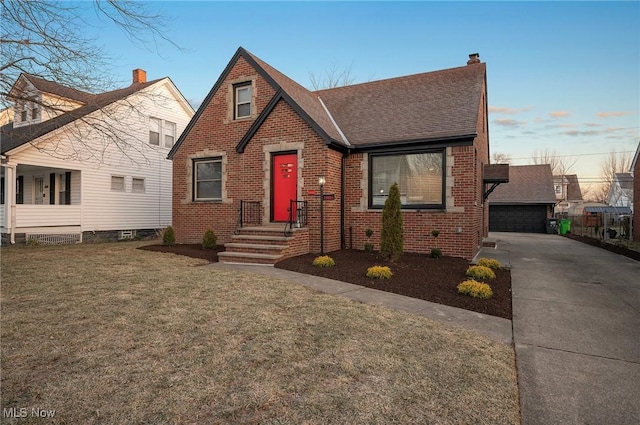 view of front facade featuring brick siding, a shingled roof, a front lawn, a chimney, and a garage