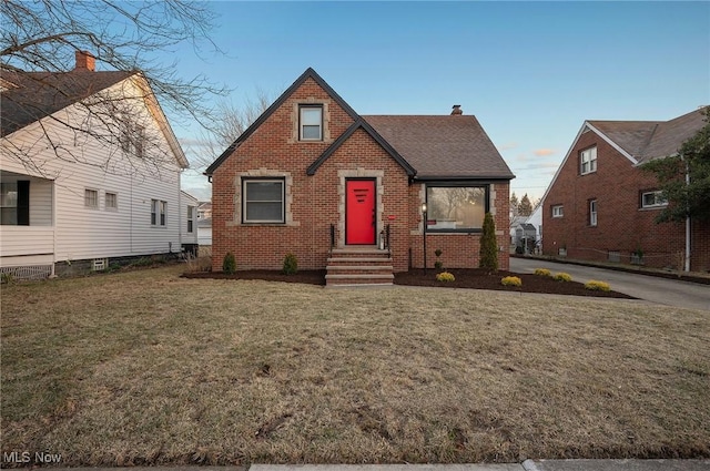 tudor home featuring a front yard, brick siding, roof with shingles, and a chimney