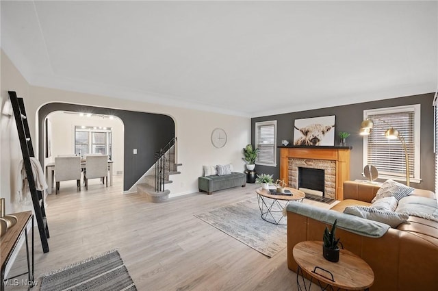 living room with stairway, baseboards, light wood-style flooring, arched walkways, and a stone fireplace