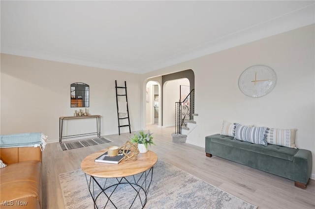 living room with stairway, arched walkways, and light wood-style flooring