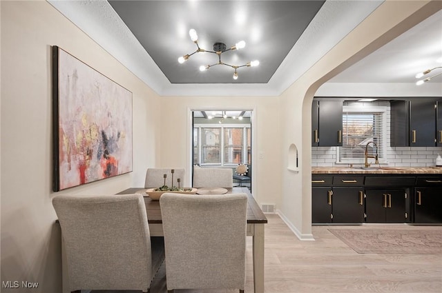 dining area featuring light wood-style floors, a raised ceiling, plenty of natural light, and arched walkways