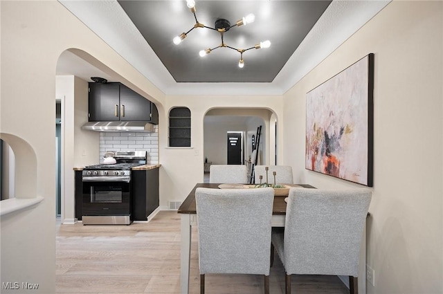 dining room with light wood-type flooring, visible vents, a tray ceiling, arched walkways, and an inviting chandelier