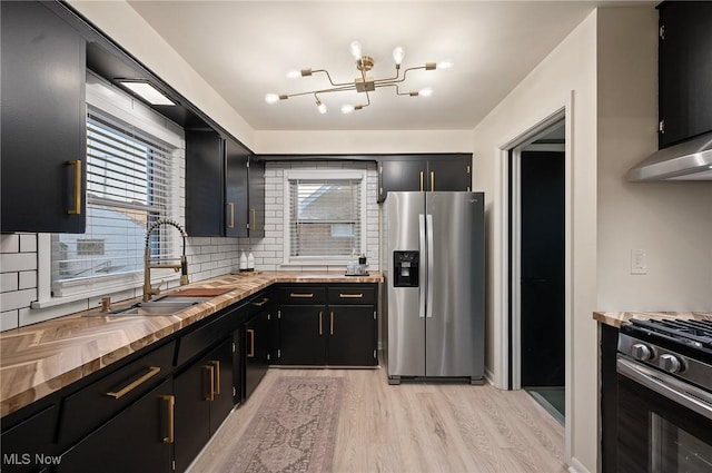 kitchen featuring an inviting chandelier, a sink, appliances with stainless steel finishes, dark cabinets, and butcher block counters