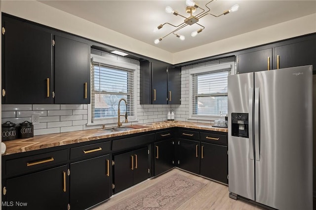 kitchen with a sink, a healthy amount of sunlight, dark cabinetry, and stainless steel fridge with ice dispenser