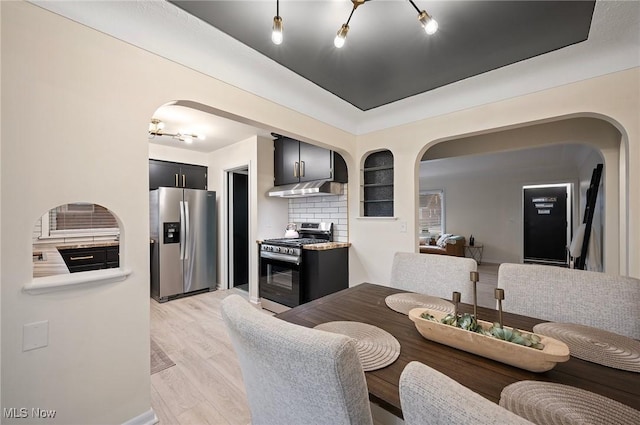 kitchen featuring arched walkways, appliances with stainless steel finishes, tasteful backsplash, and light wood-type flooring