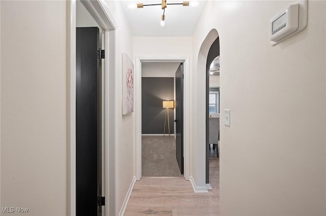 hall with baseboards, arched walkways, and light wood-type flooring