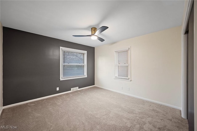 carpeted empty room with visible vents, ceiling fan, and baseboards