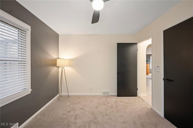 interior space with baseboards, visible vents, carpet floors, arched walkways, and ceiling fan