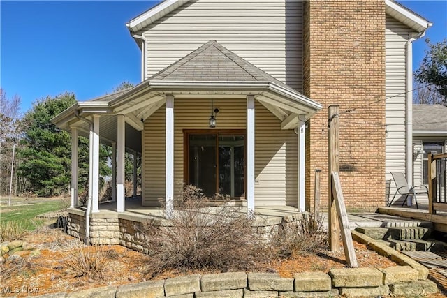 view of exterior entry featuring covered porch and roof with shingles