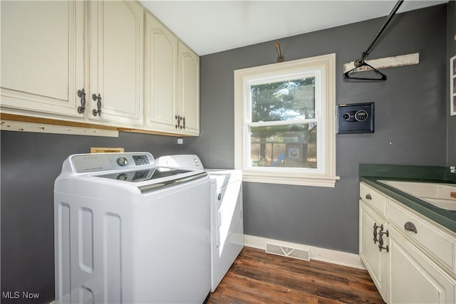 washroom with visible vents, dark wood-type flooring, a sink, washing machine and dryer, and cabinet space