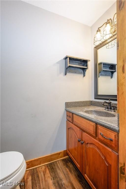 bathroom featuring baseboards, toilet, wood finished floors, and vanity