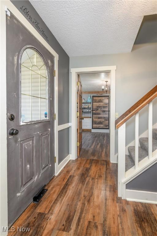 entrance foyer with a textured ceiling, stairs, baseboards, and wood finished floors